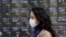 A woman walks by an electronic stock board of a securities firm in Tokyo, Wednesday, March 18, 2020.