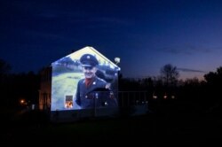 An image of veteran Chester LaPlante is projected onto the home of his son, Randy LaPlante, as he looks out a window with his wife, Nicole, and their sons, Evan and Blake, at their home in Amsterdam, N.Y., May 5, 2020.