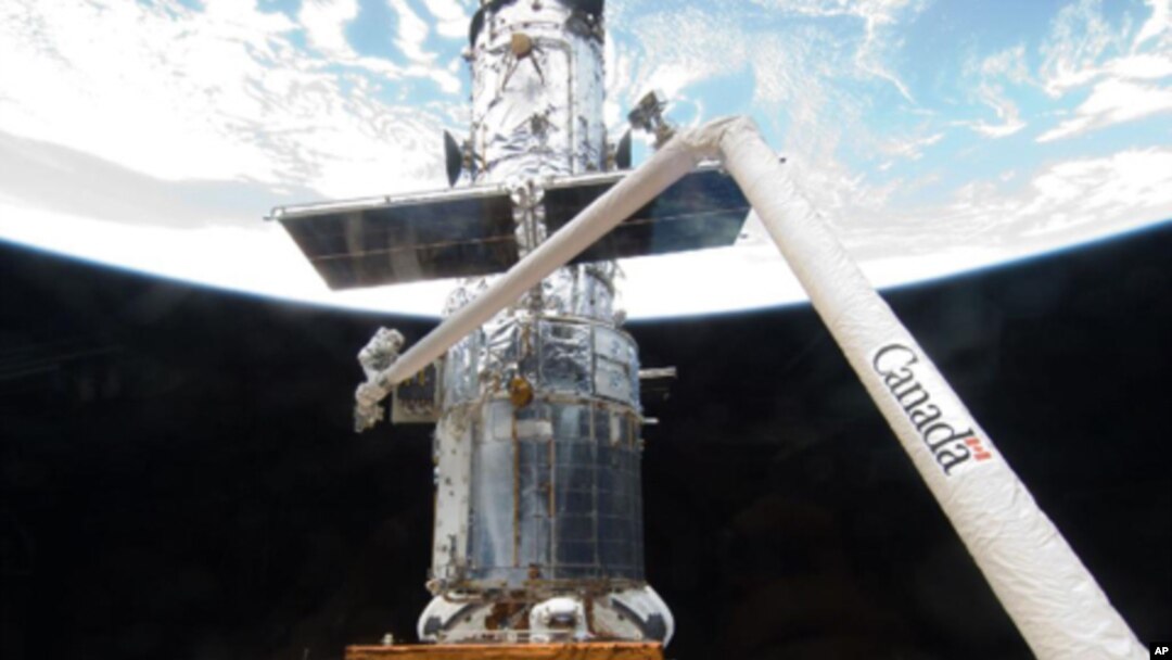 Astronaut John Grunsfeld is positioned on a foot restraint on the end of Atlantis' remote manipulator system and astronaut Andrew Feustel (bottom center) participate in the mission's fifth and final session of extravehicular activity.