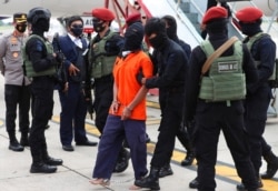 Police officers escort suspected militant Upik Lawanga, center, upon arrival at Soekarno-Hatta International Airport in Tangerang, Indonesia, Dec. 16, 2020.