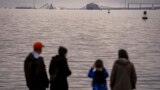 Personas en Fort Mchenry ven un barco portacontenedores apoyado contra los restos del puente Francis Scott Key el miércoles 27 de marzo de 2024 en Baltimore.