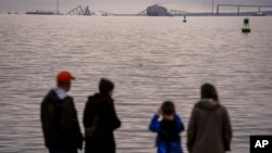 Personas en Fort Mchenry ven un barco portacontenedores apoyado contra los restos del puente Francis Scott Key el miércoles 27 de marzo de 2024 en Baltimore.