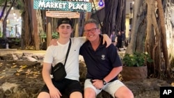 In this October 2023 photo provided by the Holdsworth family, Wayne Holdsworth sits with his son Mac on a family holiday in Hawaii. Mac took his own life last year after falling victim to an online sextortion scam. (Maggie Holdsworth via AP)