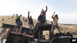 Protesters against the Dakota Access oil pipeline stand on a burned-out truck that they removed from a long-closed bridge on Sunday on a state highway near their camp in southern North Dakota, Nov. 21, 2016. 