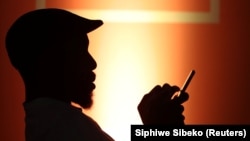 FILE: A guest types on his mobile phone as he sits below an MTN logo during the launch of its mobile money service in Johannesburg, South Africa, January 30, 2020