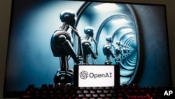 FILE - The OpenAI logo is seen displayed on a cell phone with an image on a computer screen generated by ChatGPT's Dall-E text-to-image model, Friday, Dec. 8, 2023, in Boston. (AP Photo/Michael Dwyer)