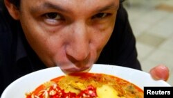 FILE - Chef Bobby Chinn sips from a bowl of Laksa, a dish popular in Singapore hawker centres, while posing for a photo in Singapore. 