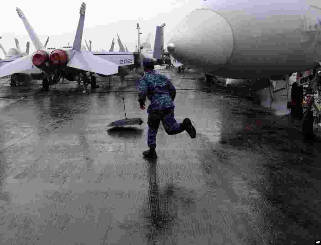 甲板上风雨交加，一名水手为记者追回吹走的雨伞