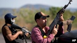 Hombres armados pertenecientes al Consejo de Autodefensas de Michoacán, montan guardia a la entrada del poblado de Antúnez, en México.