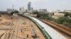 A passenger train moves past labourers working on a railway track along City Station in Karachi