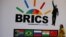 FILE - A delegate walks past a BRICS logo ahead of the 10th BRICS Summit, in Sandton, South Africa. 