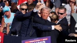 Mantan Presiden AS Donald Trump memberi isyarat dengan wajah berlumuran darah saat ia dibantu oleh personel Dinas Rahasia AS setelah ia ditembak di telinga kanannya saat kampanye di Butler Farm Show di Butler, Pennsylvania, AS, 13 Juli 2024. (Foto : REUTERS/Brendan McDermid)