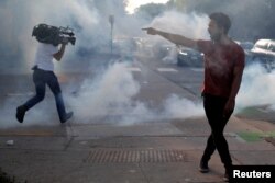 FILE - A protester argues with law enforcement officers as a reporter runs away from tear gas during a demonstration against the death in Minneapolis police custody of George Floyd, in Saint Paul, Minnesota, May 31, 2020.
