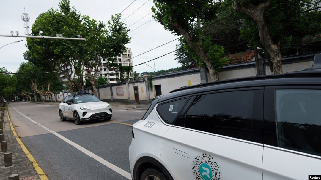 A driverless car by Apollo Go, Baidu's robotaxi service, drives past another Apollo Go robotaxi parked on the side of a road, in Wuhan, Hubei province, China, July 19, 2024.