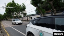 A driverless car by Apollo Go, Baidu's robotaxi service, drives past another Apollo Go robotaxi parked on the side of a road, in Wuhan, Hubei province, China, July 19, 2024.