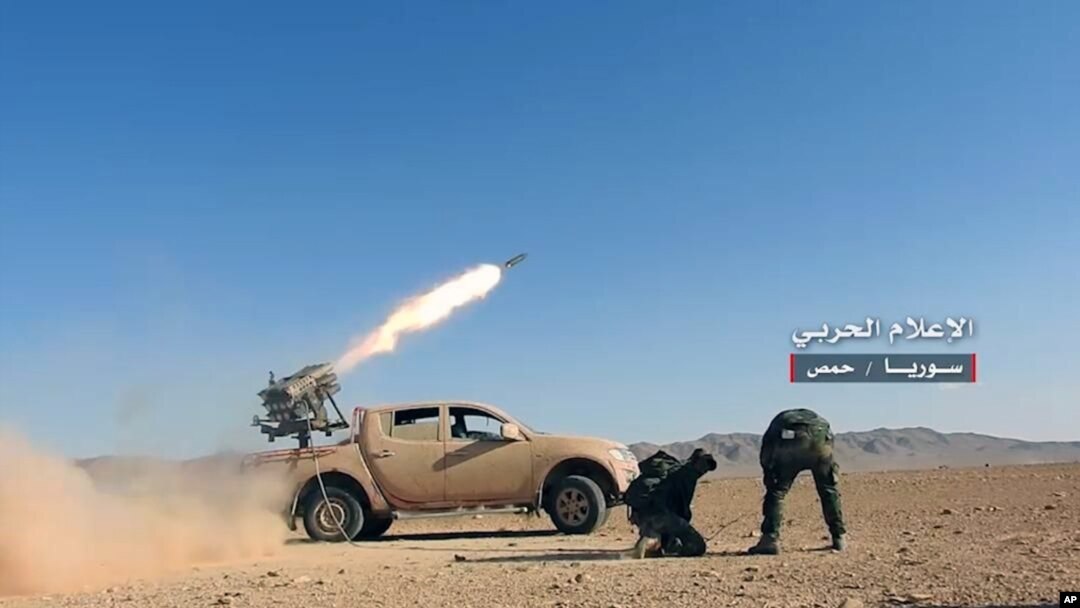 FILE - May 25, 2017 photo provided by the government-controlled Syrian Central Military Media, shows Syrian government troops firing multiple launcher rockets at insurgent group's position, in the Syrian province of Homs.