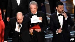 Jordan Horowitz shows the envelope revealing "Moonlight" as the true winner of best picture at the Oscars, Feb. 26, 2017, at the Dolby Theatre in Los Angeles. . Host Jimmy Kimmel and presenter Warren Beatty look on from right.