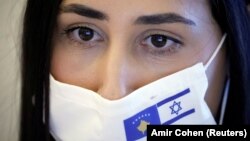 Seorang perempuan mengenakan masker bergambar bendera Israel dan Kosovo dalam upacara virtual pembukaan hubungan diplomatik antara kedua negara, di Kementerian Luar Negeri Israel, di Yerusalem, 1 Februari 2021. (Foto: Amir Cohen/Reuters) 