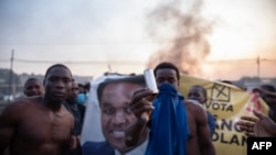 Manifestantes do bairro de Maxaquene manifestam-se em Maputo, a 24 de outubro de 2024, enquanto mostram uma lata de gás lacrimogéneo gasta em frente a um cartaz com a fotografia do candidato presidencial do Partido Otimista para o Desenvolvimento, na oposição