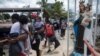 Migrantes haitianos caminan junto a la estatua de la Virgen María mientras abordan un bote hacia Capurgana cerca de la frontera con Panamá, en Necoclí, Colombia, el miércoles 28 de julio de 2021.