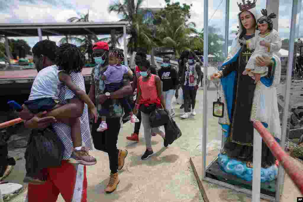 Migrantes haitianos pasan junto a la estatua de la Virgen Mar&#237;a mientras abordan un barco hacia Capurgan&#225;.