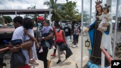 Migrantes haitianos caminan junto a la estatua de la Virgen María mientras abordan un bote hacia Capurgana cerca de la frontera con Panamá, en Necoclí, Colombia, el miércoles 28 de julio de 2021.