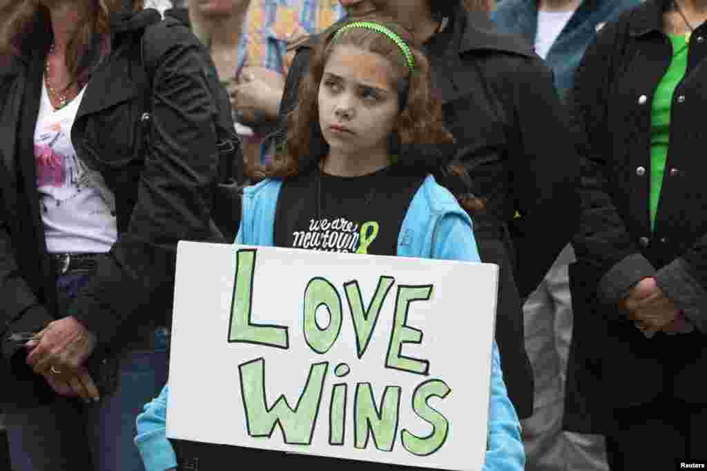 Seorang anak perempuan memegang poster dalam acara peringatan enam bulan tragedi penembakan di Newtown di luar balaikota Newtown, Connecticut. 