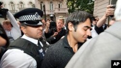 Pakistani cricketer Salman Butt (R) is escorted by a policeman through a scrum of media outside the Pakistan High Commission in London, 2 Sept. 2010.