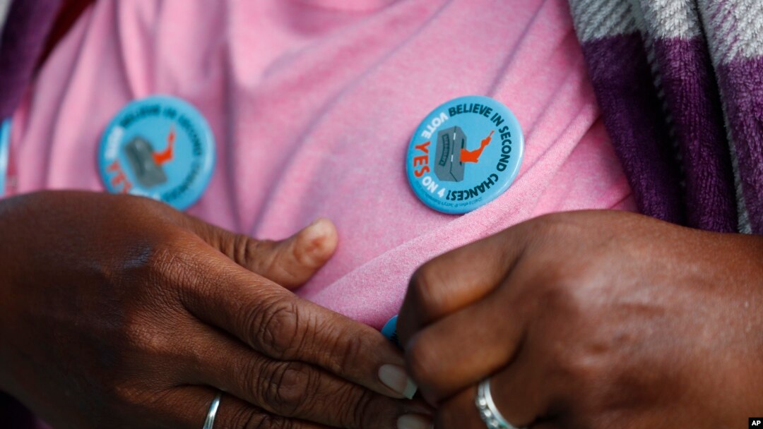 Yvette Demerit puts on a pin-back button in support of Amendment 4 at the Ben & Jerry's "Yes on 4" truck where people learned about Amendment 4 and eat free ice cream in Miami, Oct. 22, 2018.