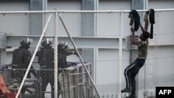 FILE - A youth tries to climb over the border fence in the Spanish exclave of Ceuta bordering Morocco on April 13, 2021. 