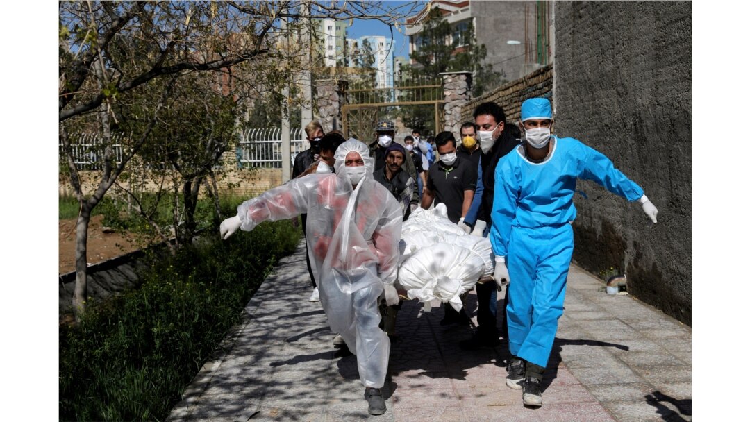 People wearing protective clothing carry the body of a victim who died after being infected with the new coronavirus, at a cemetery just outside Tehran, Iran, March 30, 2020.