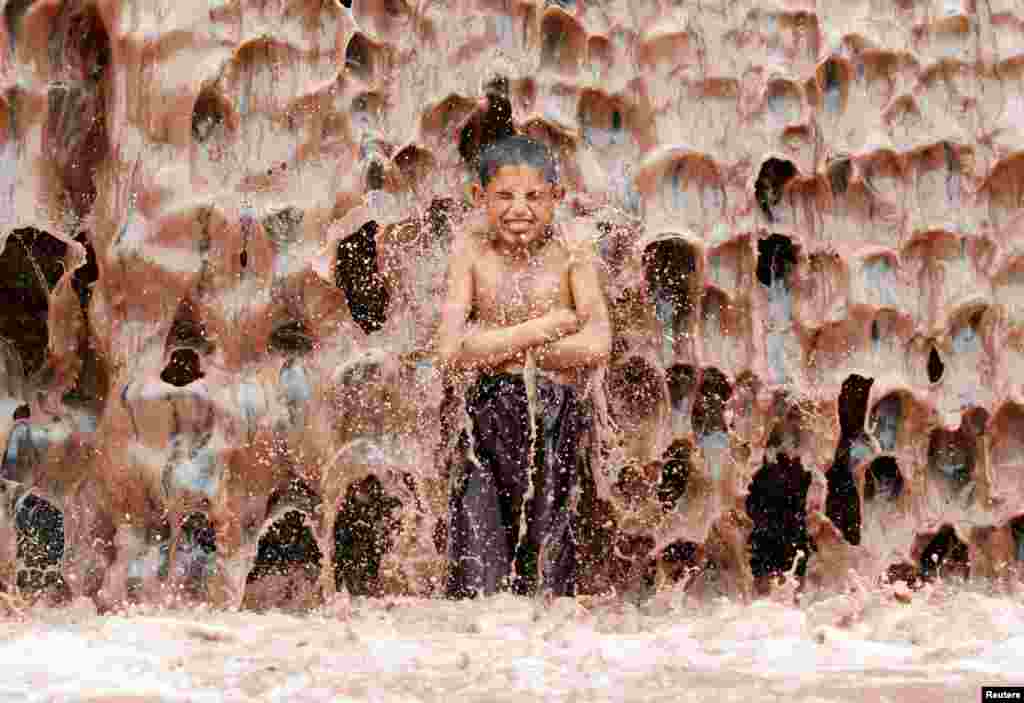 Seorang anak laki-laki mendinginkan diri di bawah air terjun di pinggiran Jalalabad, Afghanistan.