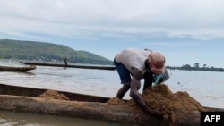 FILE - Saturnin Yenzia organises sand in his pirogue on the Ubangi river in Bangui on November 8, 2023.