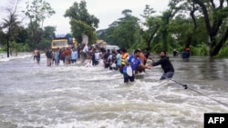 Warga berjalan di tengah banjir di Feni, 22 Agustus 2024. Banjir yang dipicu oleh hujan deras telah menggenangi sebagian wilayah dataran rendah Bangladesh, menambah tantangan bagi pemerintahan baru setelah berminggu-minggu terjadi kekacauan politik. (AFP)