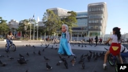 Una artista disfrazada como Elsa de Arendelle, el personaje de Disney, camina por la plaza frente al Palacio Nacional en el centro histórico de San Salvador, El Salvador, el miércoles 24 de enero de 2024. (Foto AP/Salvador Meléndez).