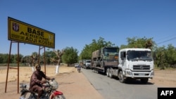 A man on a motorcycle drives past trucks carrying French army vehicles and equipment leaving Adji Kossei air base for the port of Douala in Cameroon prior to the complete departure of the French army from Chad, in N'Djamena, Jan. 29, 2025.