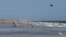 A helicopter flies close to the water as vacationers relax on the beach in Oak Island, North Carolina, June 15, 2015.