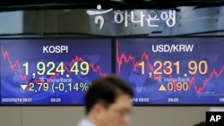A currency trader walks near the screens showing the KOSPI left, and the foreign exchange rate between U.S. dollar in Seoul, South Korea, May 18, 2020. 