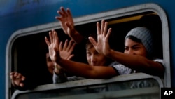 Asylum-seekers wave out of a train window as their train departs for the Hungarian border with Austria in Budapest, Hungary, Sept. 6, 2015. 