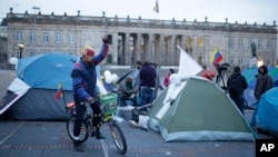 FILE - A cyclist raises his arm next to students camping to ask for peace at the main square in Bogota, Colombia, Oct. 7, 2016. 