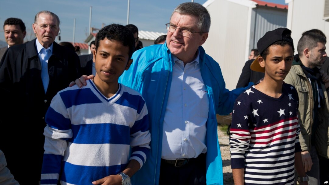 IOC President Thomas Bach, center, walks with two young refugees with former IOC President Jacques Rogge in the background, during their visit to a refugee camp in Athens, Greece, Jan, 28, 2016.