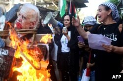 FILE - A woman speaks as an image of US President Joe Biden is burnt during a protest in the Ain al-Hilweh Palestinian refugee camp near the southern Lebanese port city of Sidon on October 18, 2023, as the US President visited neighbouring Israel, and a day afte