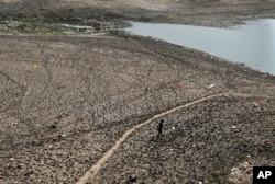 FILE - A man walks across a dried patch of the river Yamuna as water level reduces drastically following heat wave to in New Delhi on May 2, 2022. (AP Photo/Manish Swarup, File)