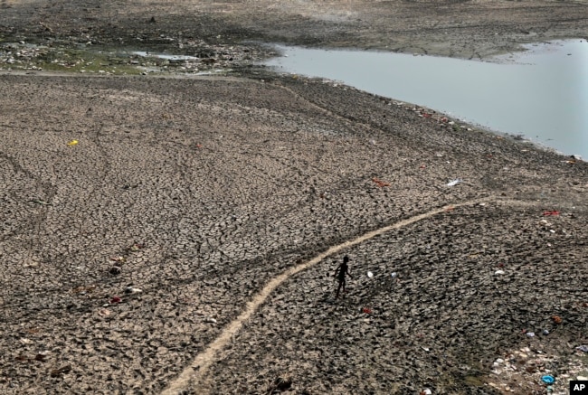 FILE - A man walks across a dried patch of the river Yamuna as water level reduces drastically following heat wave to in New Delhi, May 2, 2022. In India, it's record heat connected to climate change that caused deaths and ruined crops. (AP Photo/Manish Swarup, File)