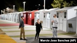 Workers talk to a person who is living at the village (at right) in front of tiny homes for the homeless, February 25, 2021, in the North Hollywood part of Los Angeles. (AP Photo/Marcio Jose Sanchez)