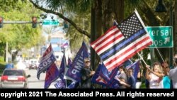 Partidarios del expresidente Donald Trump ondean banderas afuera del centro de convenciones de Orlando, Florida, donde se realiza la Conferencia de Conservadores de Acción Política, CPAC, el domingo 28 de febrero de 2021.
