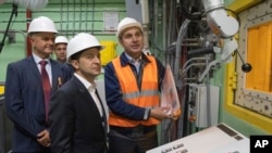 Ukrainian President Volodymyr Zelenskiy, foreground, visits the "new safe confinement" shelter that spans the remains of the Chernobyl nuclear power plant's Reactor No. 4, in Chernobyl, Ukraine, July 10, 2019.