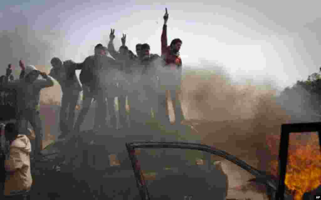 Libyan rebels celebrate on top of burning cars after Libyan leader Moammar Gadhafi's forces where pushed back from Benghazi, eastern Libya, Saturday, March 19, 2011. Explosions shook the Libyan city of Benghazi early on Saturday while a fighter jet was he