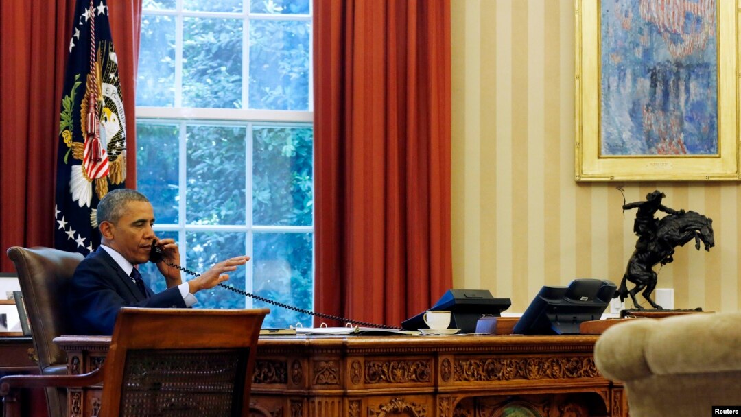 FILE - President Barack Obama is photographed through the window as he speaks in the Oval Office during a conference call at the White House in Washington, June 2, 2014.