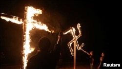 FILE - Members of a white nationalist group burn a swastika and cross outside Atkins, Arkansas, March 9, 2019.